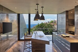 A modern kitchen with a large island, a flat-screen TV, and a view of the ocean.