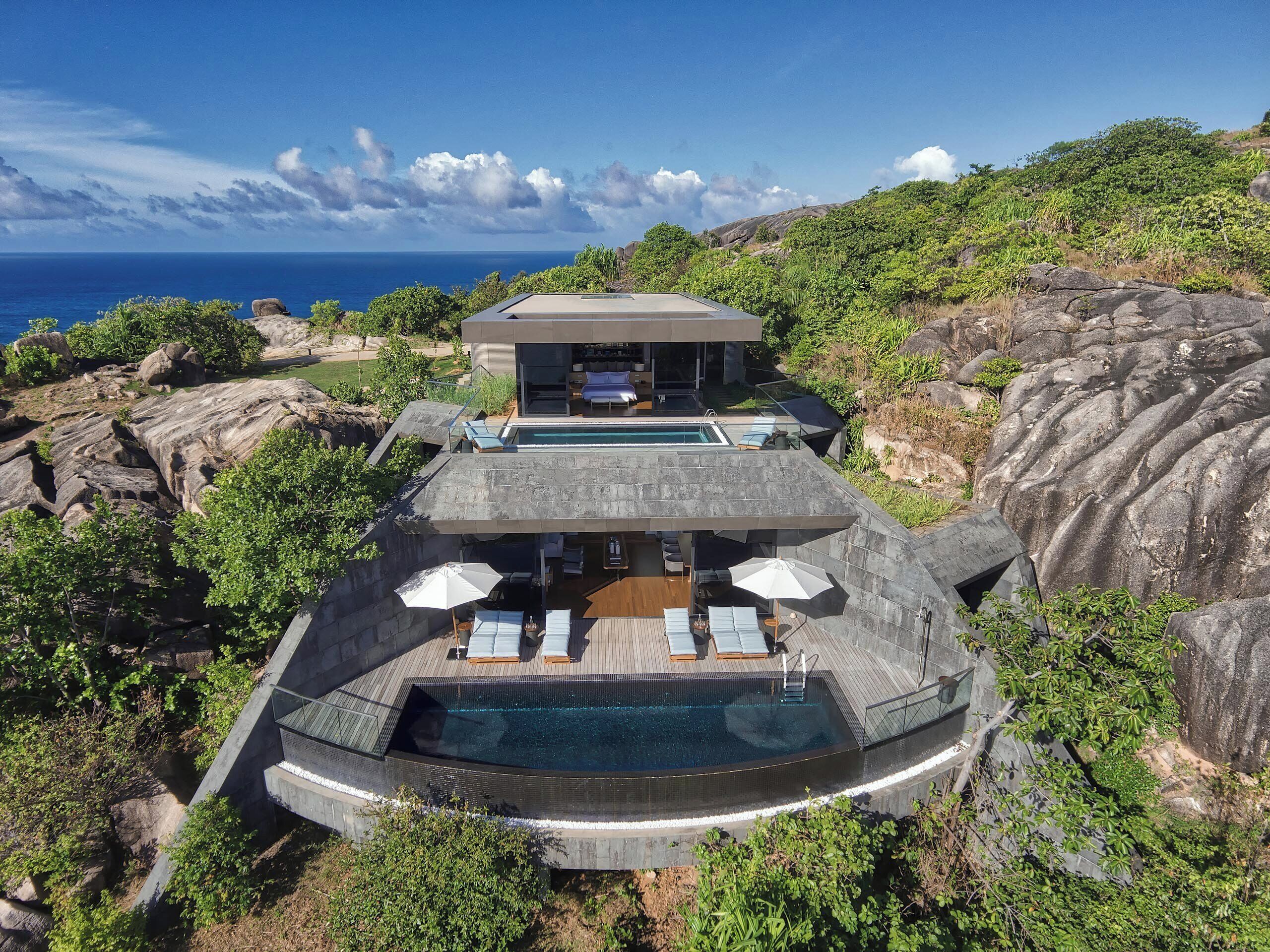 Une maison moderne avec une piscine, entourée d’un paysage rocheux et de verdure.