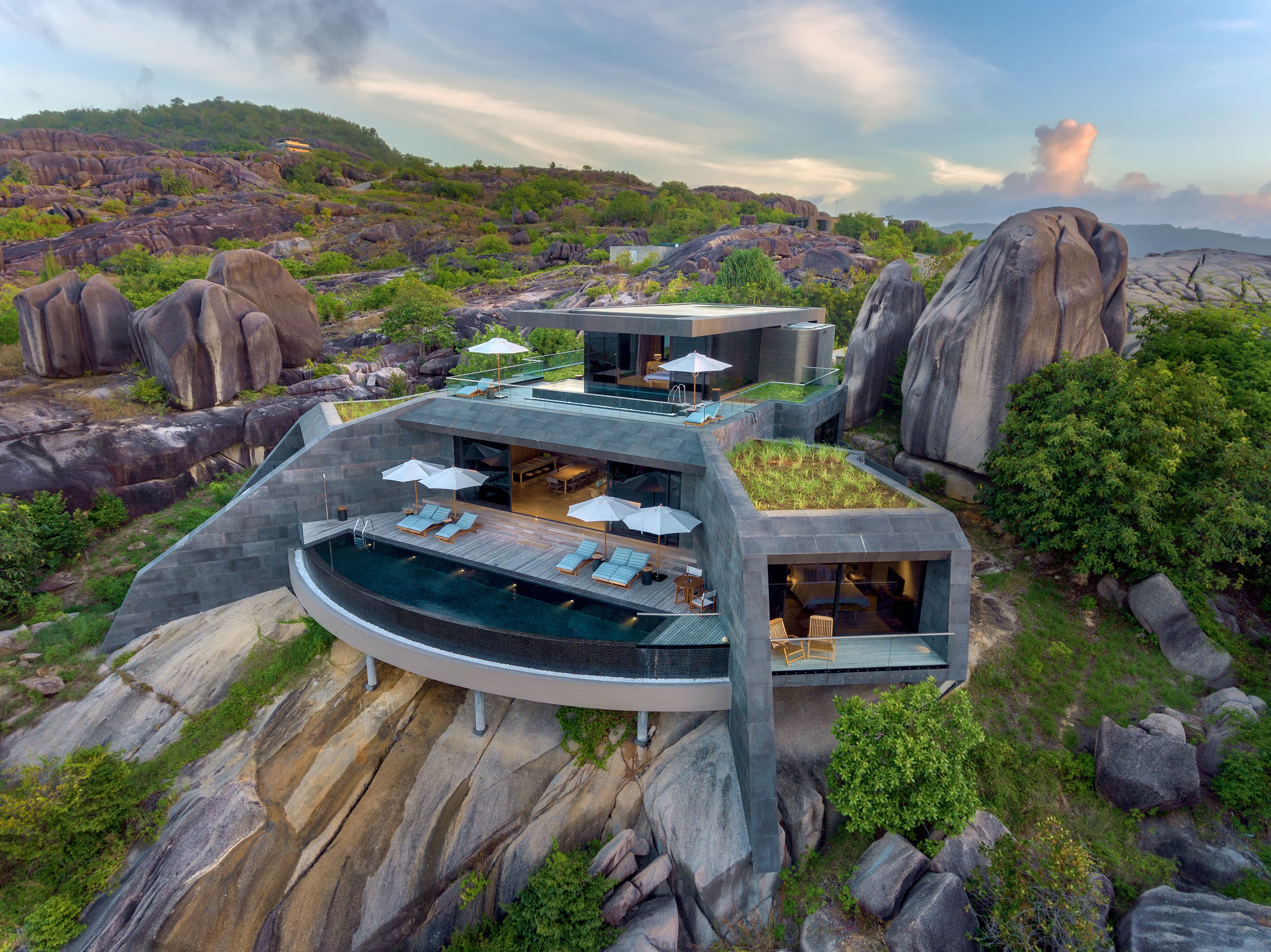 Una villa moderna con piscina infinita en la azotea, mobiliario de exterior y un exuberante jardín.