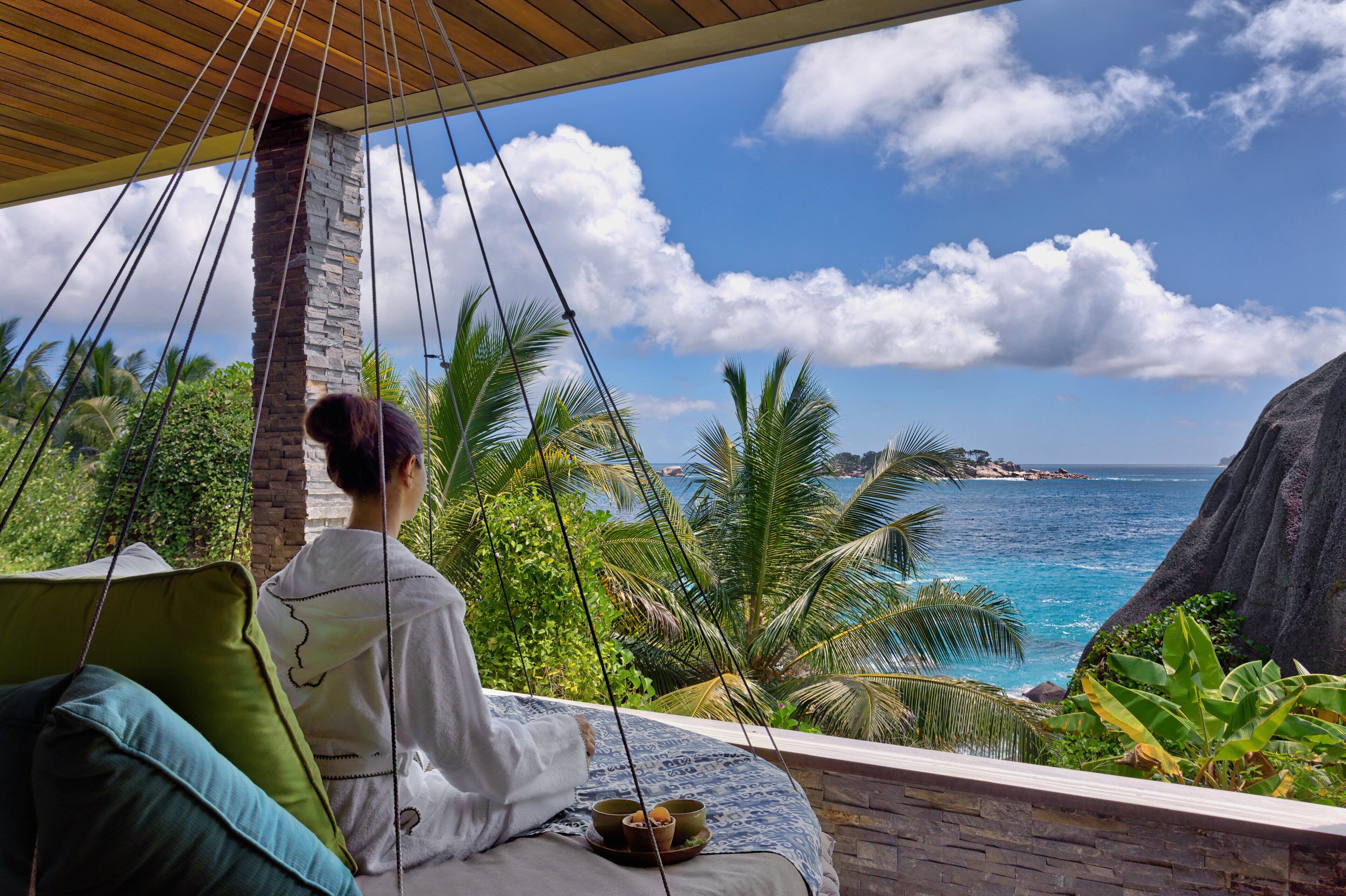 A hammock chair overlooking a tropical beach with palm trees and a clear blue sky.
