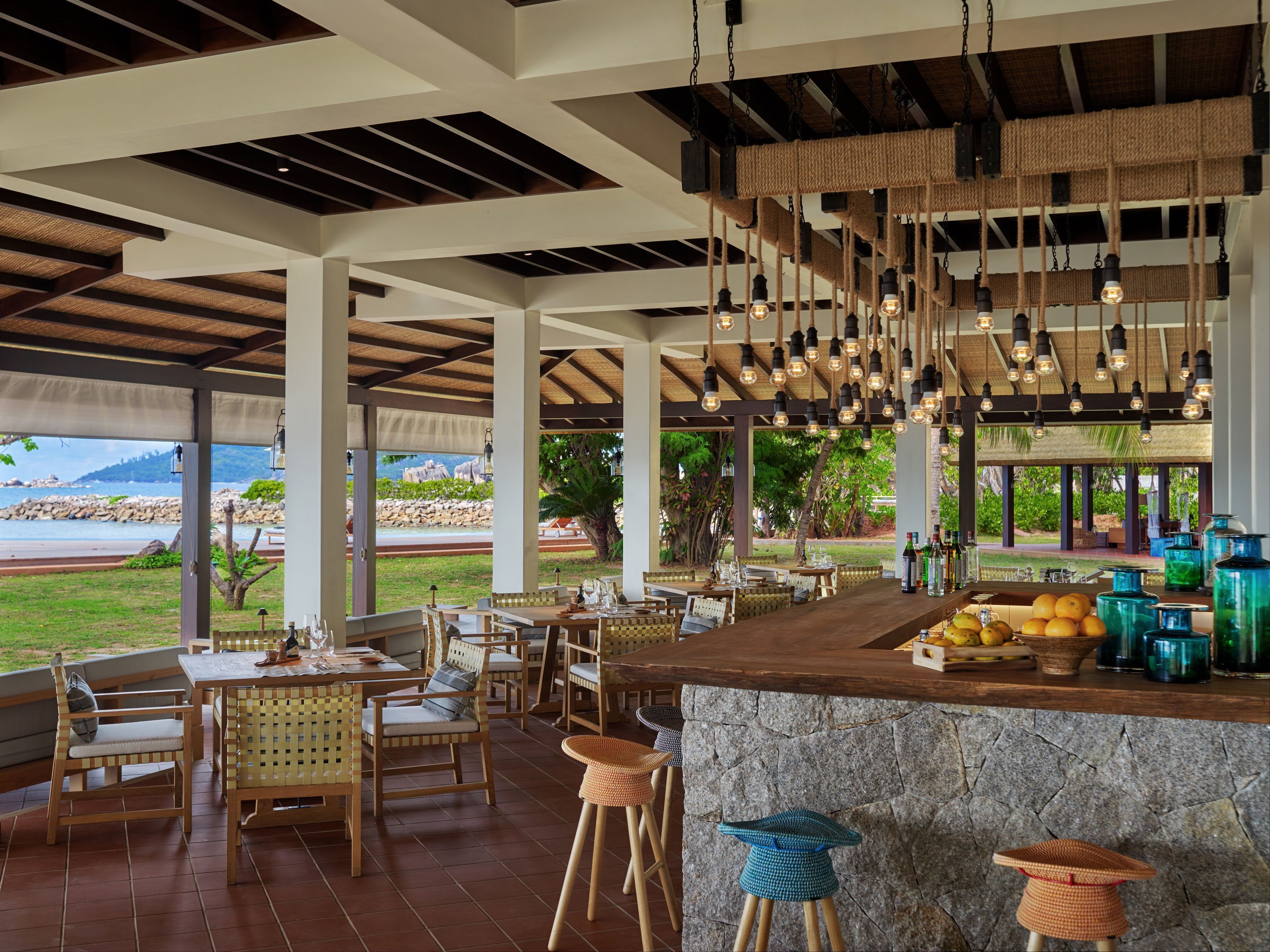 A restaurant with a stone bar, wicker chairs, and hanging light fixtures.