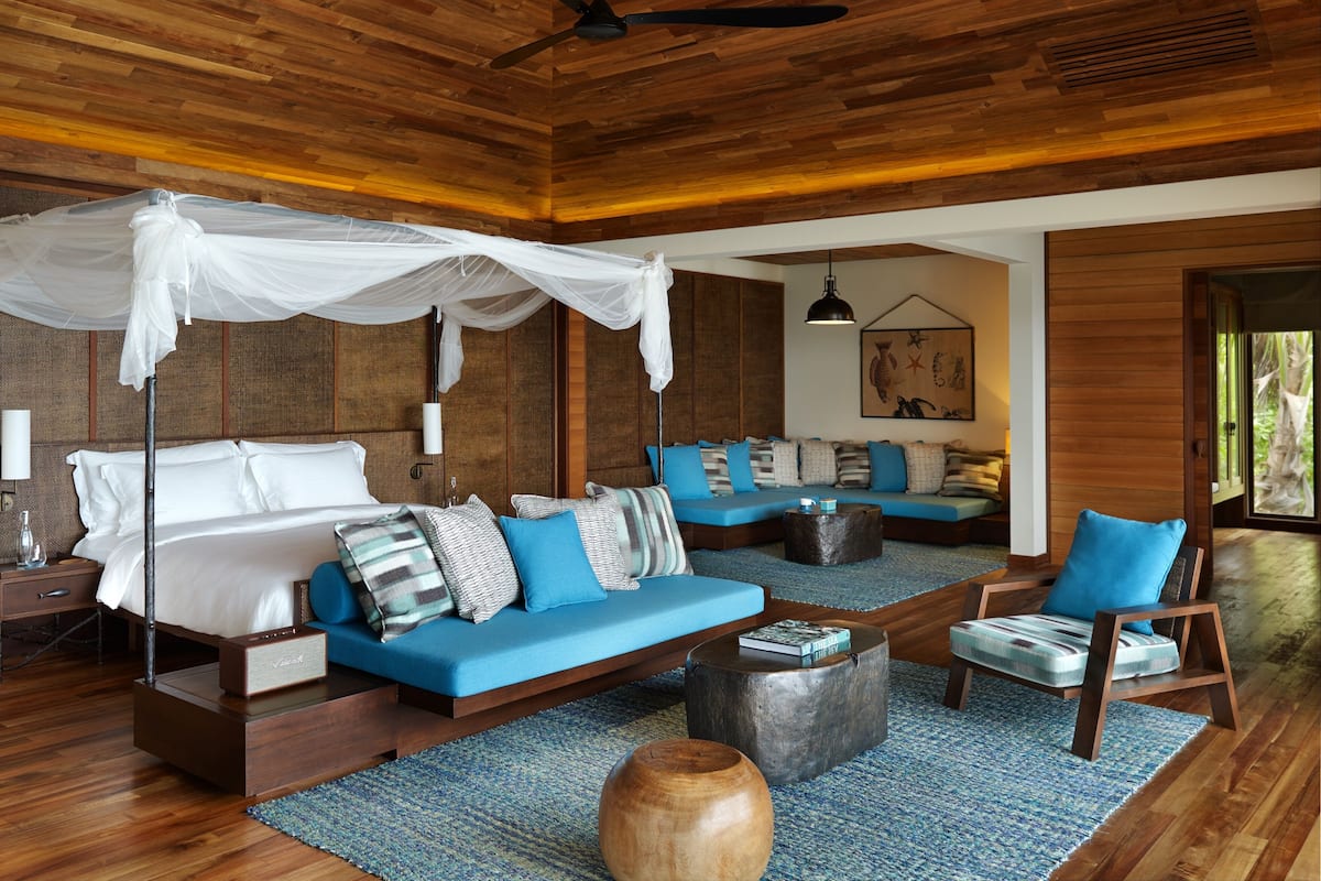 Una habitación amplia con cama, sofás azules, una mesa de centro de madera y una silla de madera.
