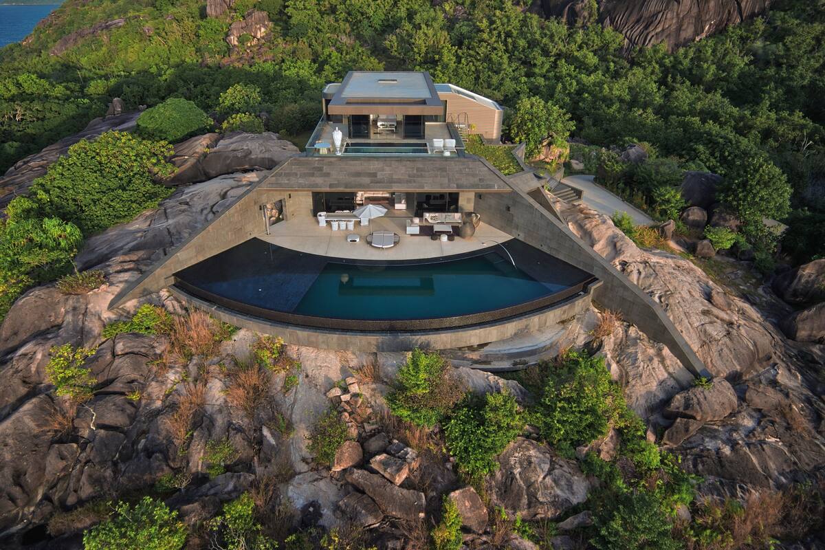 Una casa moderna con piscina circular rodeada de rocas, con vistas a una zona boscosa.