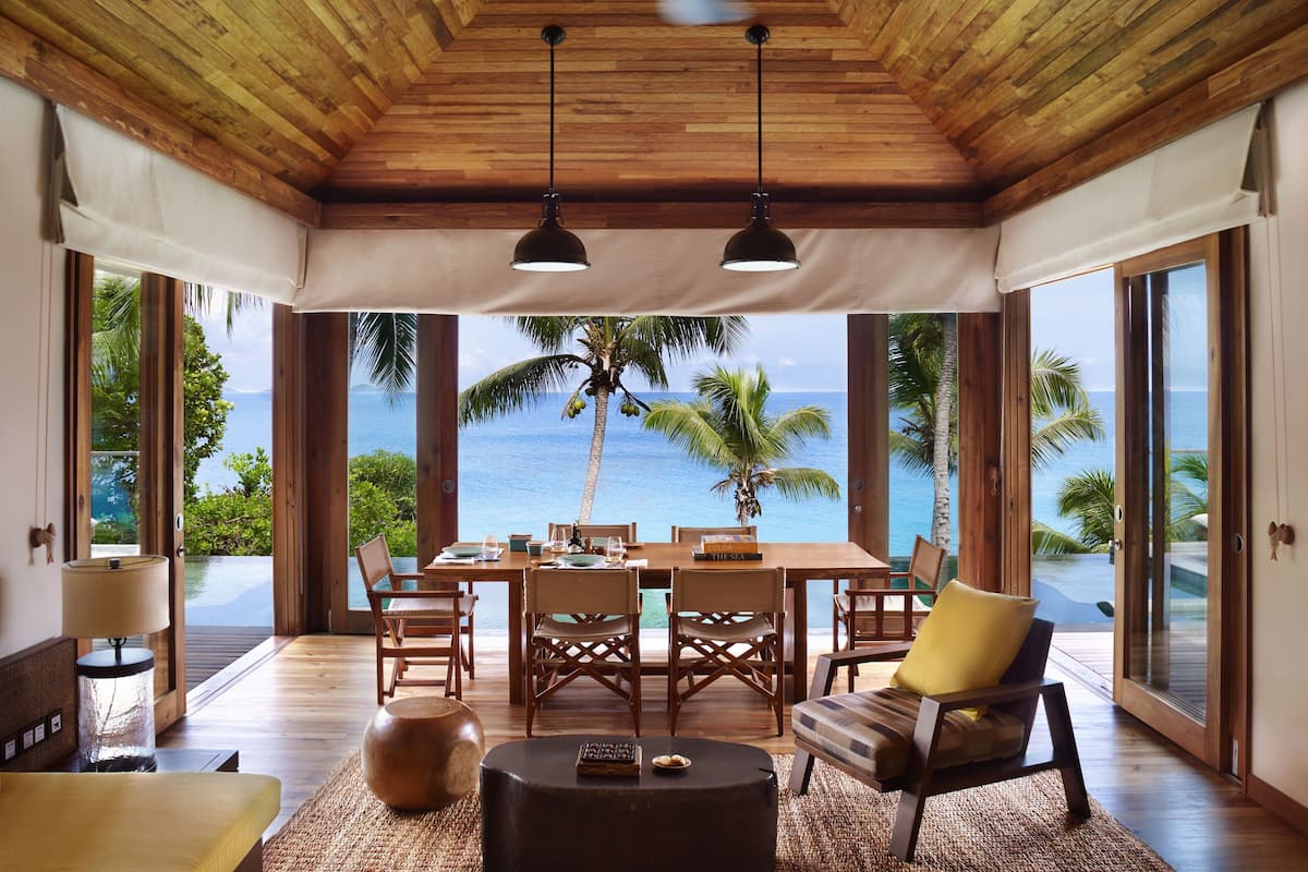 Una habitación amplia con techo de madera, ventanas grandes y vista al océano.