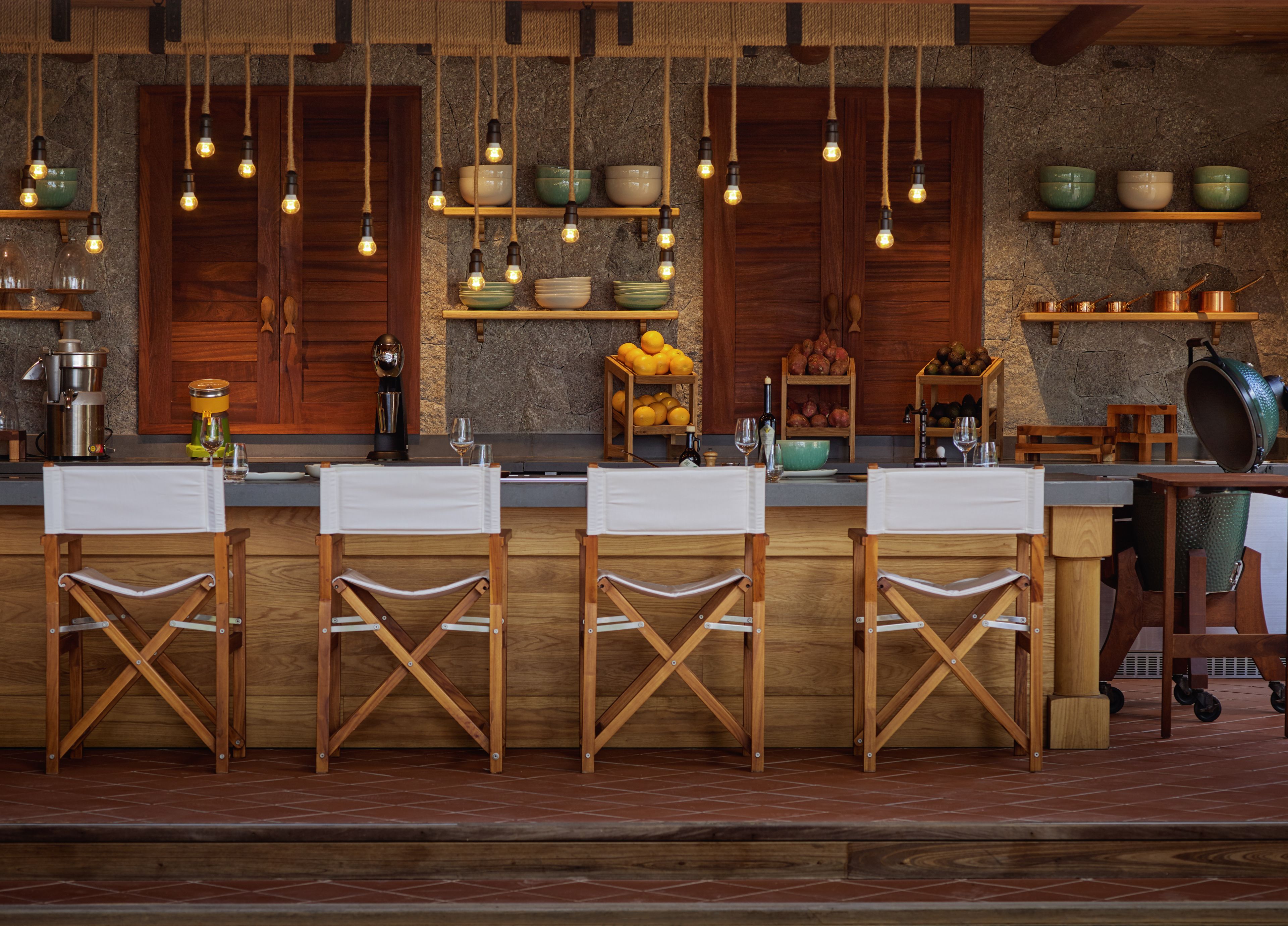 Una cocina rústica con taburetes de madera, luces colgantes y estantes con cuencos y frutas.