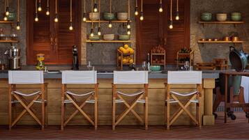 Una cocina rústica con taburetes de madera, luces colgantes y estantes con cuencos y frutas.