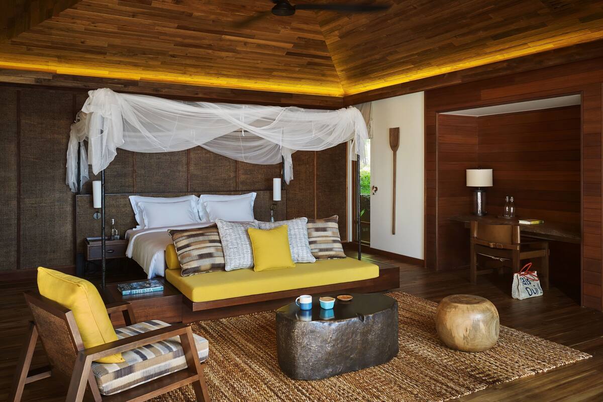 Un dormitorio con cama, mesita de noche, silla y una pequeña mesa con lámpara.