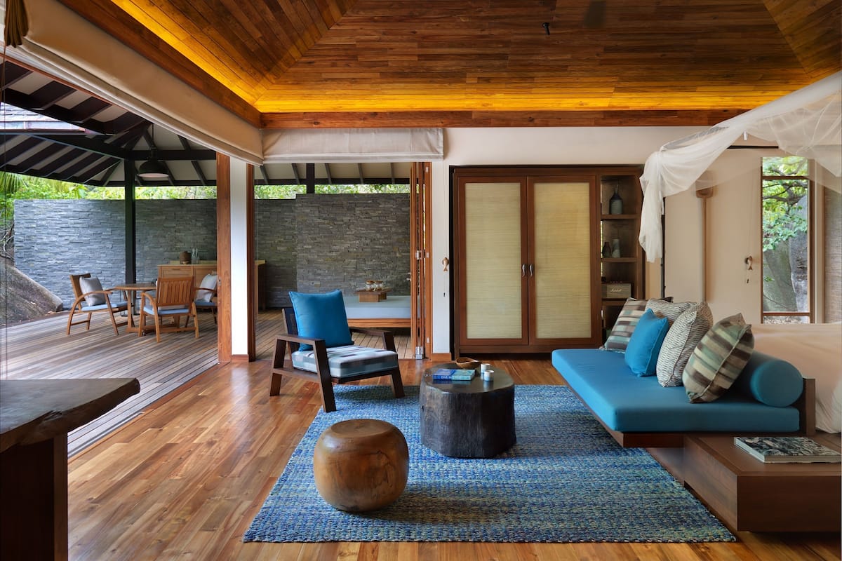 Una habitación amplia con techo de madera, un sofá azul con cojines, una mesa de centro de madera y un taburete grande de madera.