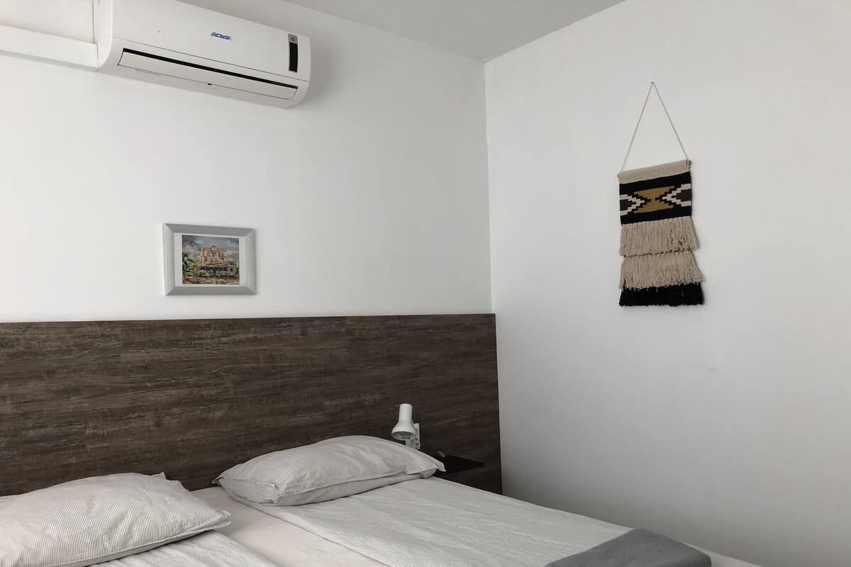 Habitación de hotel con cama, aire acondicionado de pared, un cuadro enmarco y un tapiz.