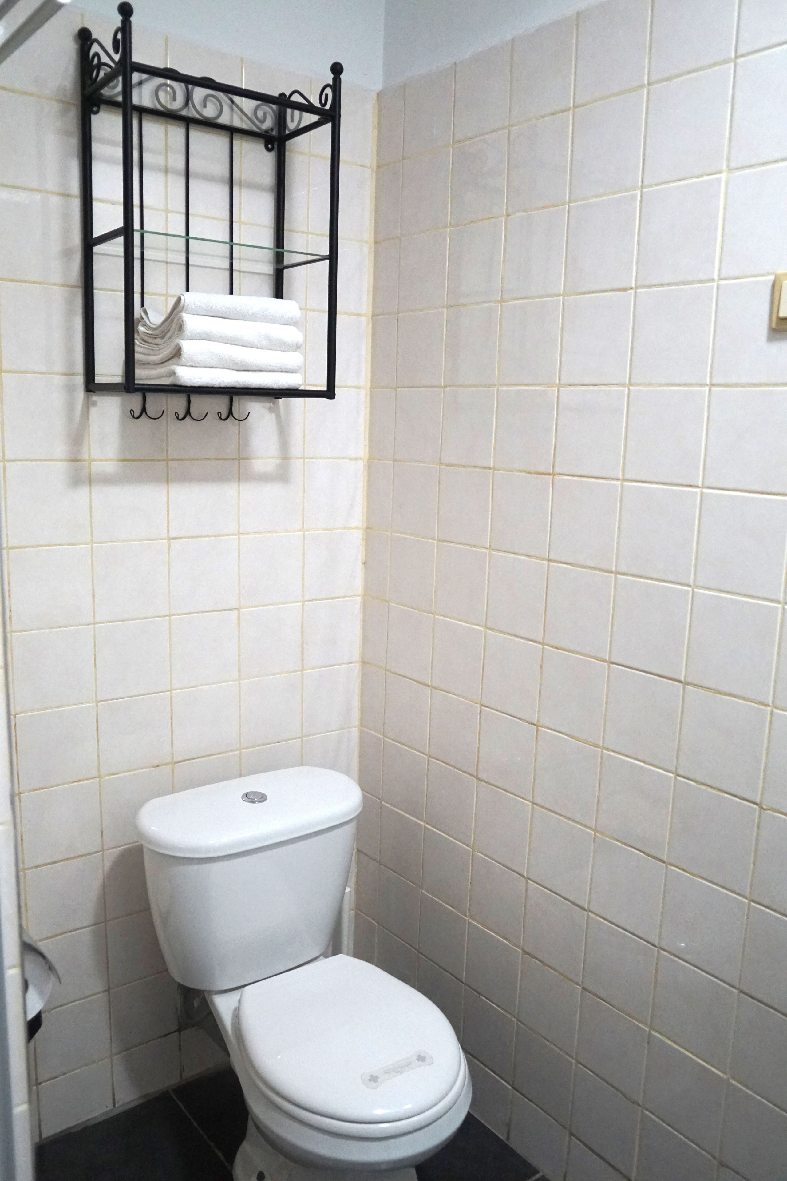 Ein Badezimmer mit weißer Toilette, einem Handtuchhalter mit gefalteten Handtüchern und gefliesten Wänden.