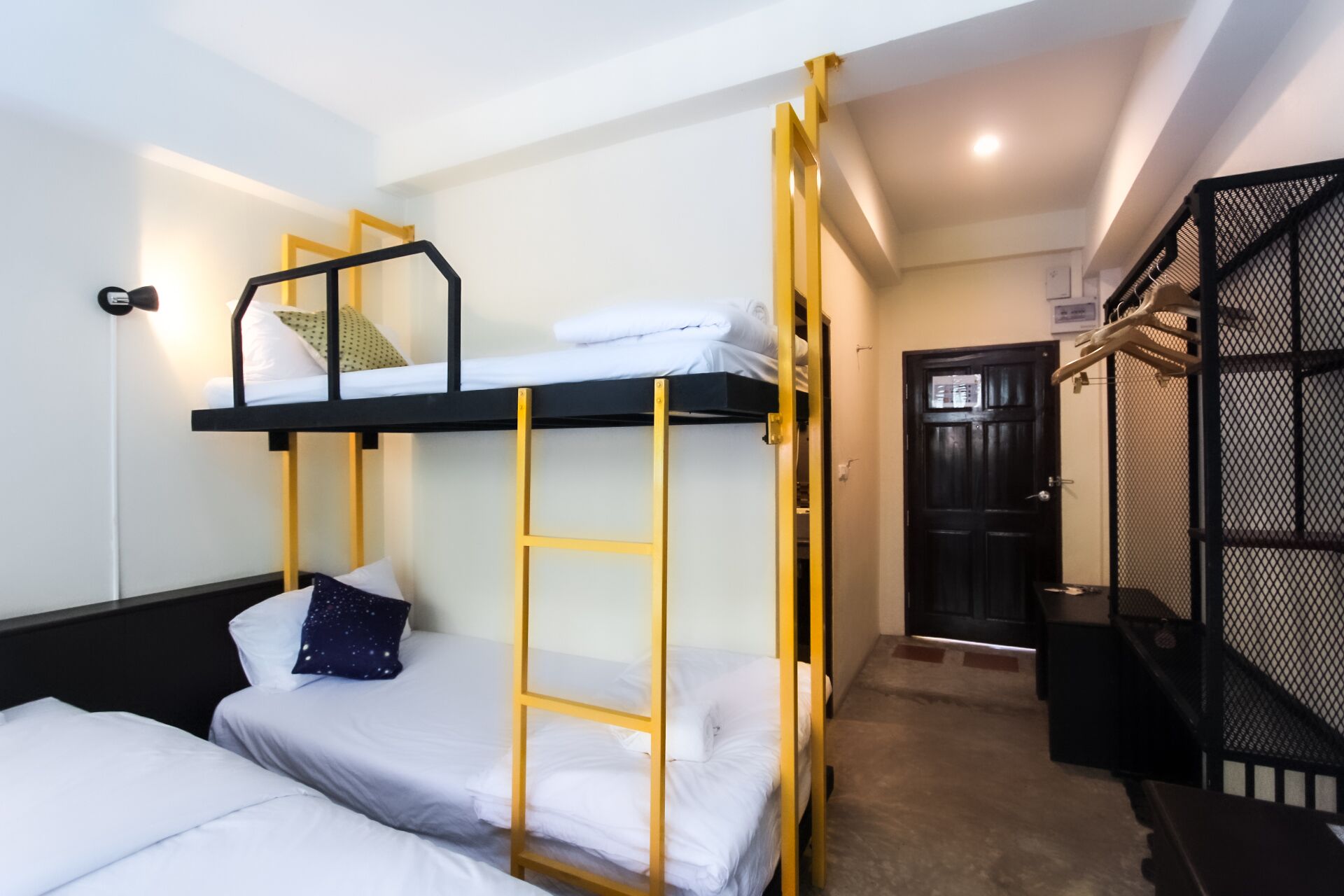A bunk bed room with a black and yellow frame, a white door, and a staircase with a black railing.