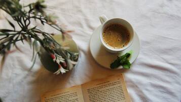 Una taza de café sobre un platito con una ramita de menta, junto a un libro sobre una superficie blanca.