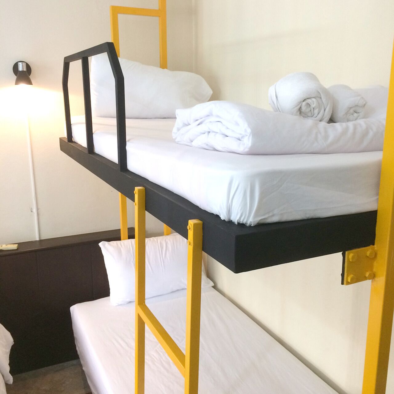 Uma cama beliche com roupa de cama branca e grades amarelas num quarto com uma mesa de cabeceira e uma luminária.