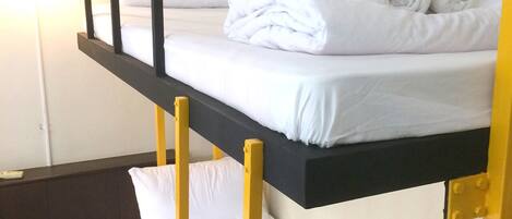 A bunk bed with white bedding and yellow railings in a room with a single bedside table and a lamp.