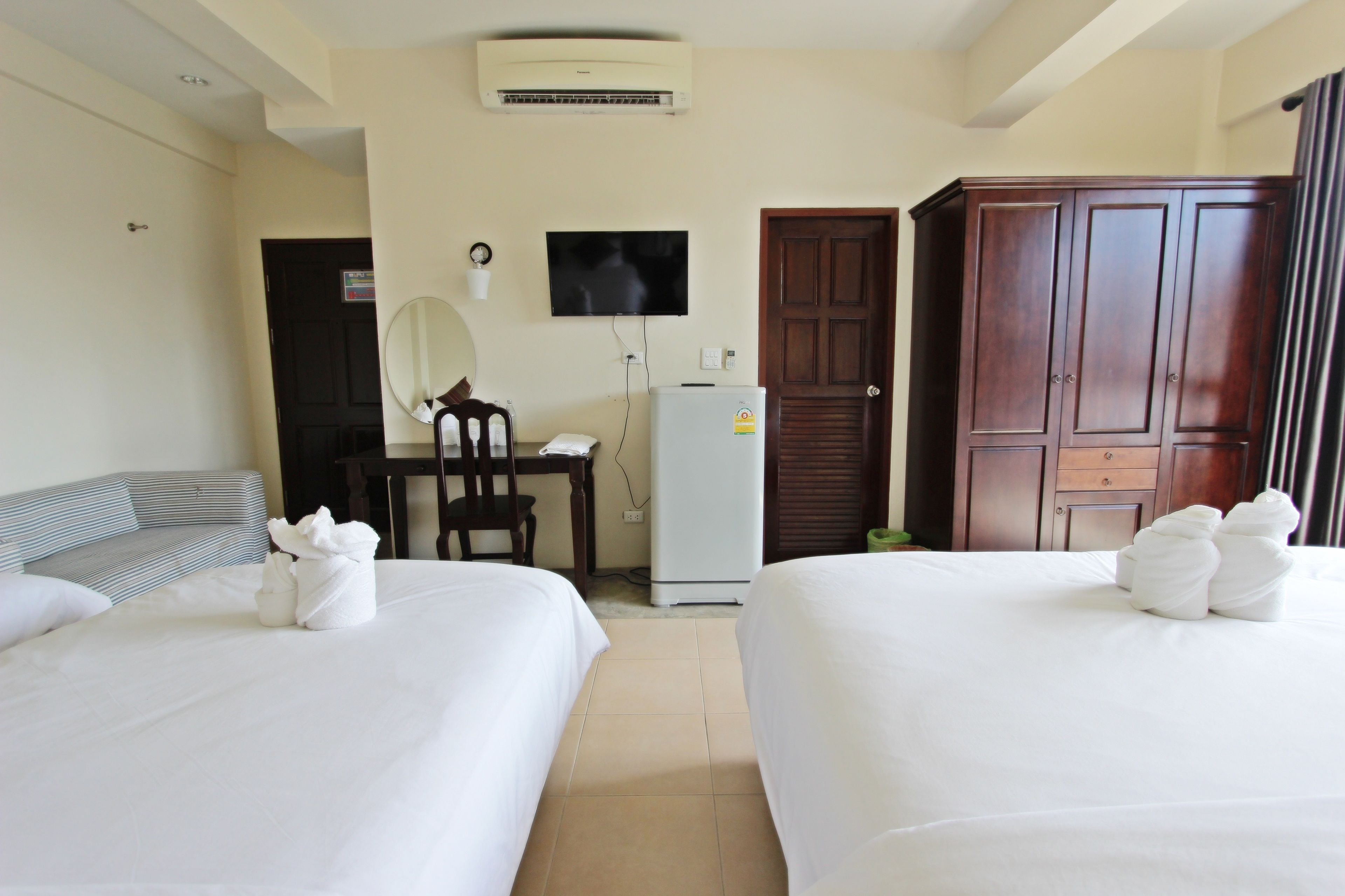 A hotel room with two beds, a desk, a television, an air conditioner, and a wardrobe.