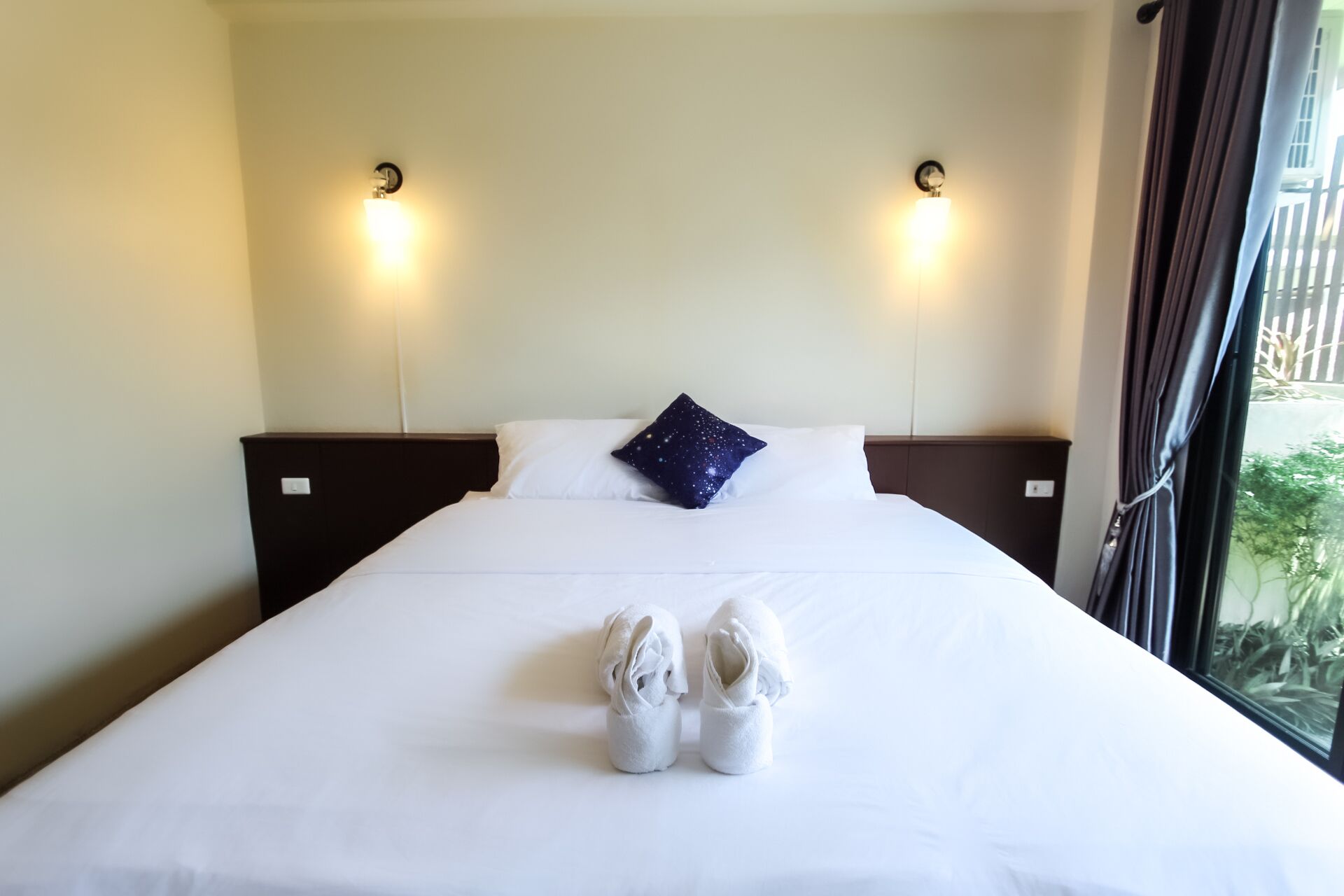 A hotel room with a neatly made bed, two bedside lamps, and a pair of towels folded on the bed.