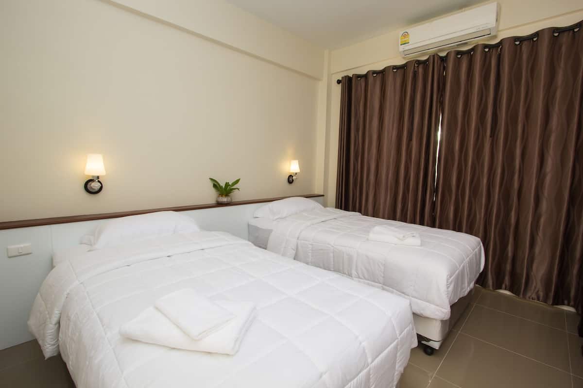 Quarto de hotel com duas camas, um vaso de planta, luminárias na parede e uma janela grande com cortinas.