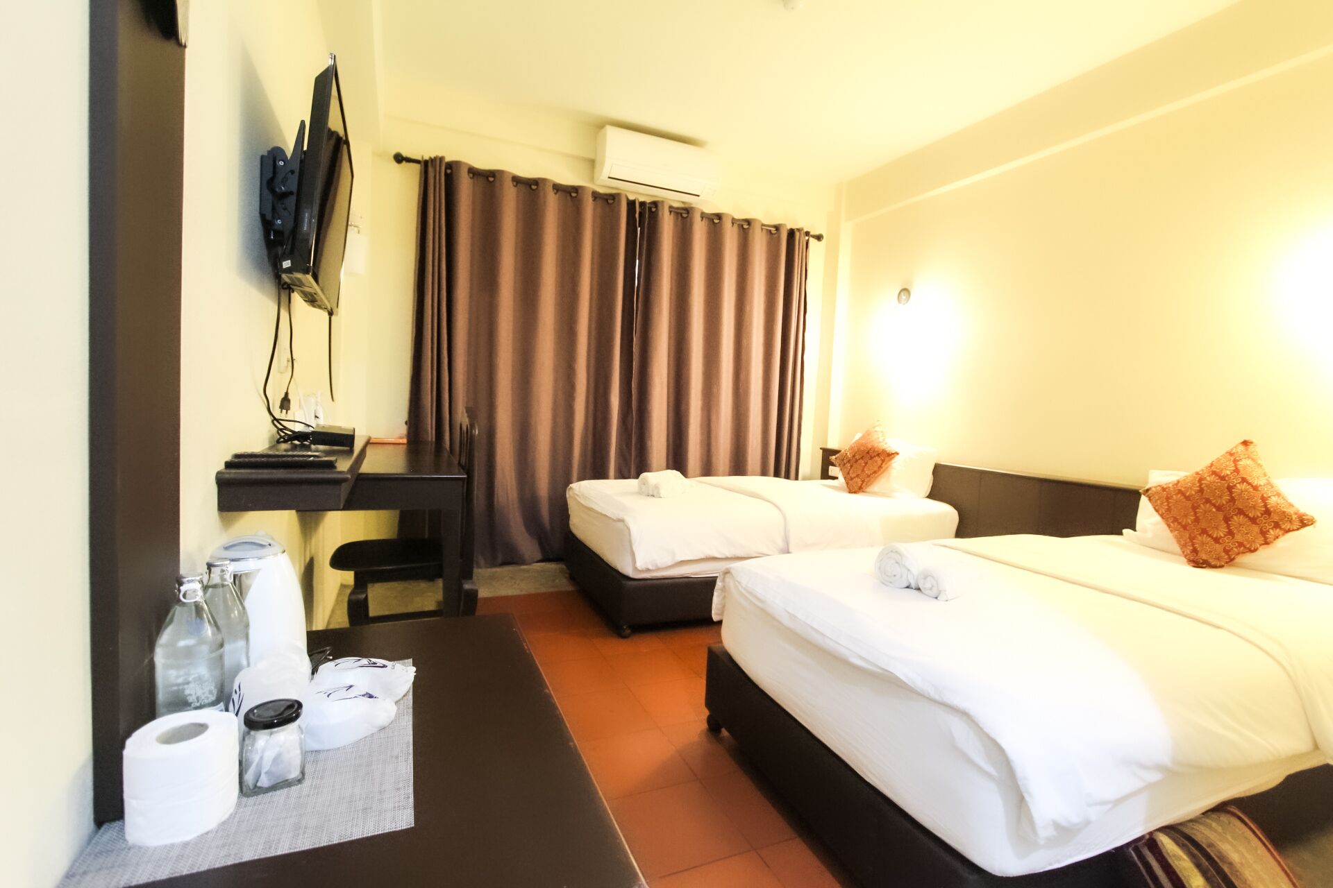 Habitación de hotel con dos camas, un escritorio con televisor y un área de baño.