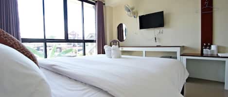Habitación de hotel con una cama grande, un escritorio con televisor de pantalla plana, un espejo y una ventana con cortinas.