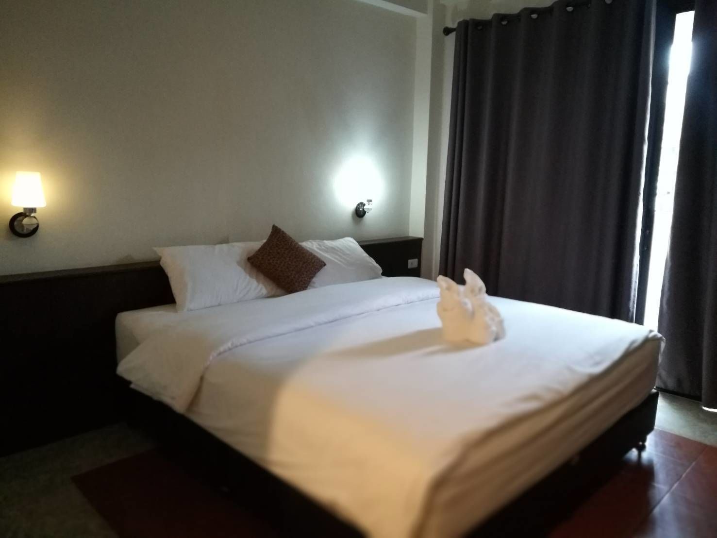 A hotel room with a neatly made bed, two bedside lamps, and a window with curtains.
