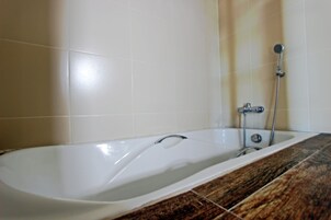 Un baño con una bañera blanca, un cabezal de ducha y una pared con azulejos.