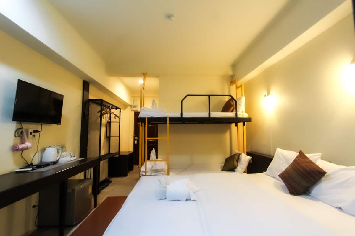 Quarto de hotel com uma cama de solteiro, uma escrivaninha com computador, televisão e guarda-roupa.