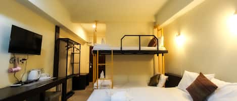 Una habitación de hotel con literas, un escritorio con una computadora, un televisor y un armario.