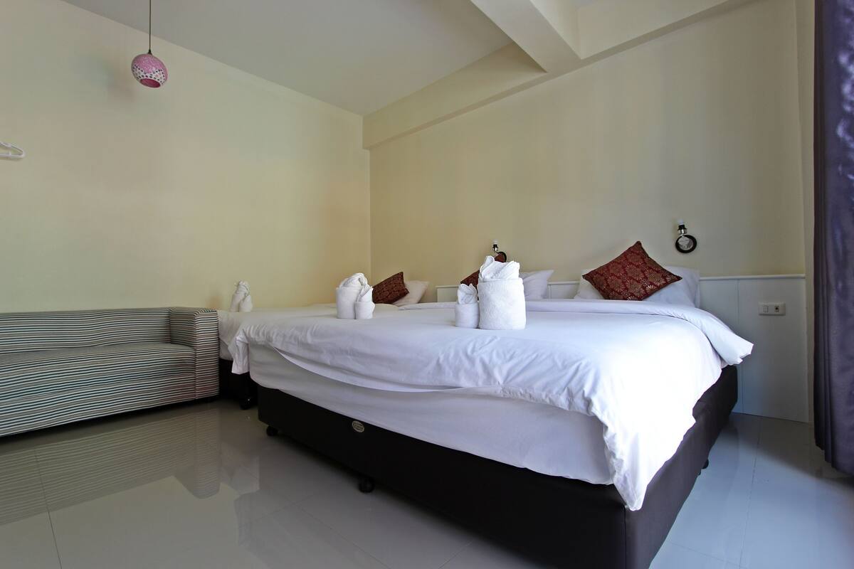 Quarto de hotel com uma cama grande, um sofá e um candeeiro suspenso.