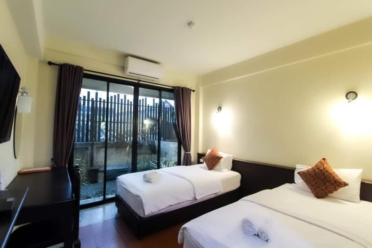 Quarto de hotel com duas camas, uma escrivaninha, janela com cortinas e vista para uma cerca.
