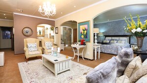 A spacious living room with a chandelier, a sofa set, a coffee table, and a painting on the wall.
