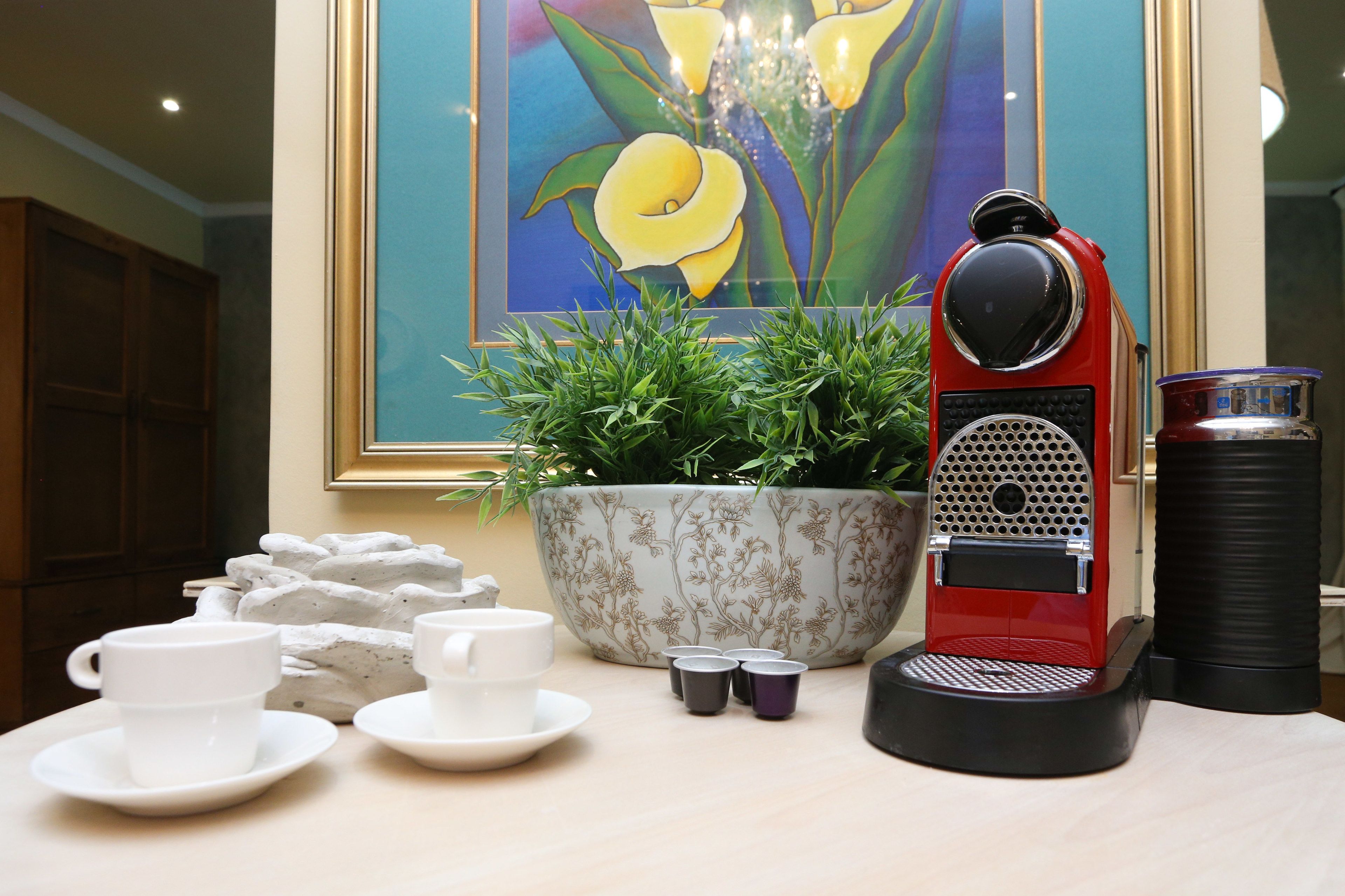 A coffee station with a red espresso machine, a large floral pot, and several cups and saucers.
