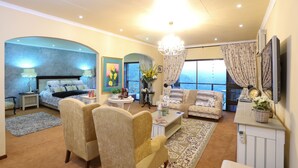 A spacious living area with a large bed, two armchairs, a coffee table, and a television.