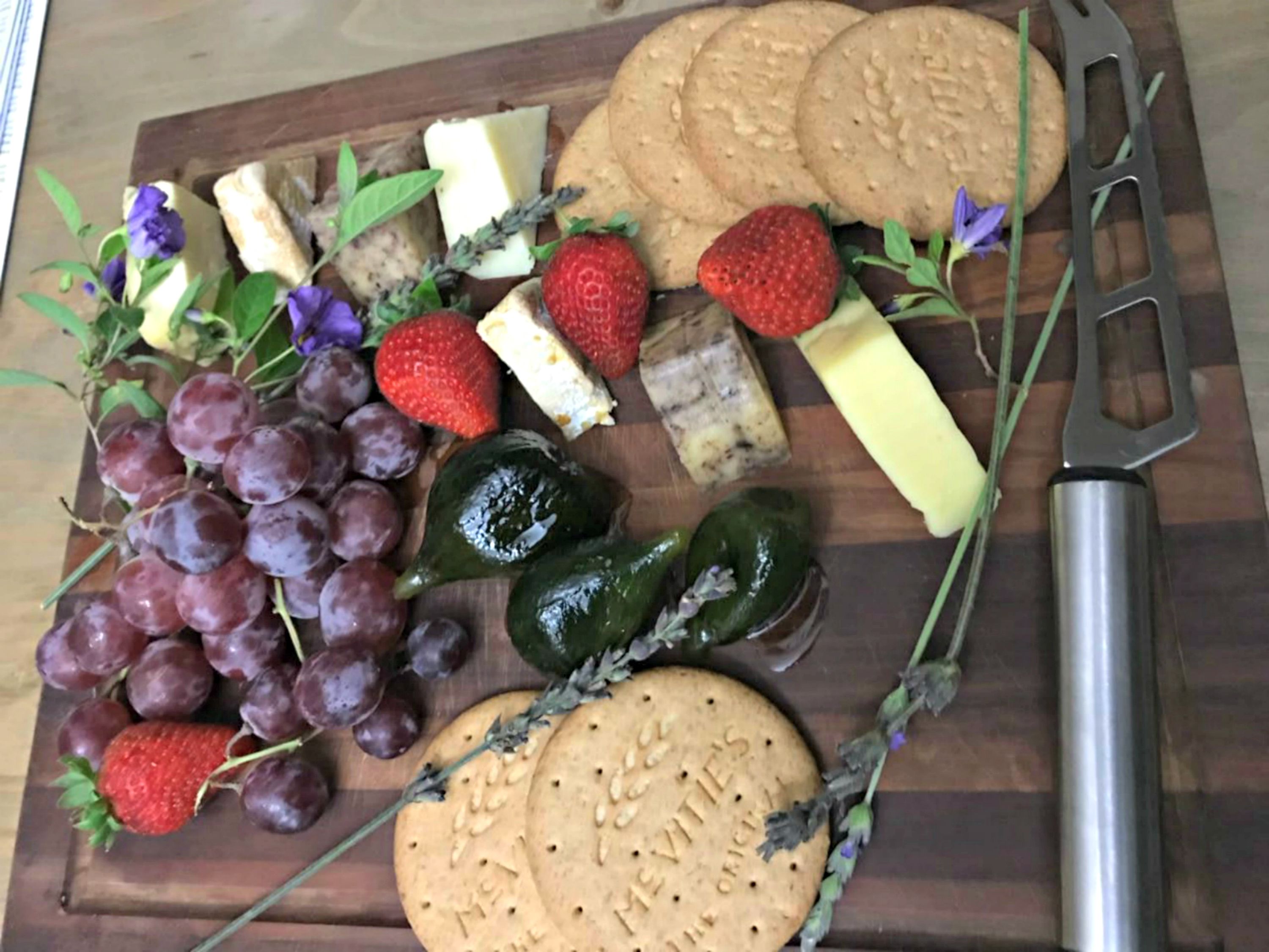 A wooden board with various food items including grapes, strawberries, cheese, and crackers.