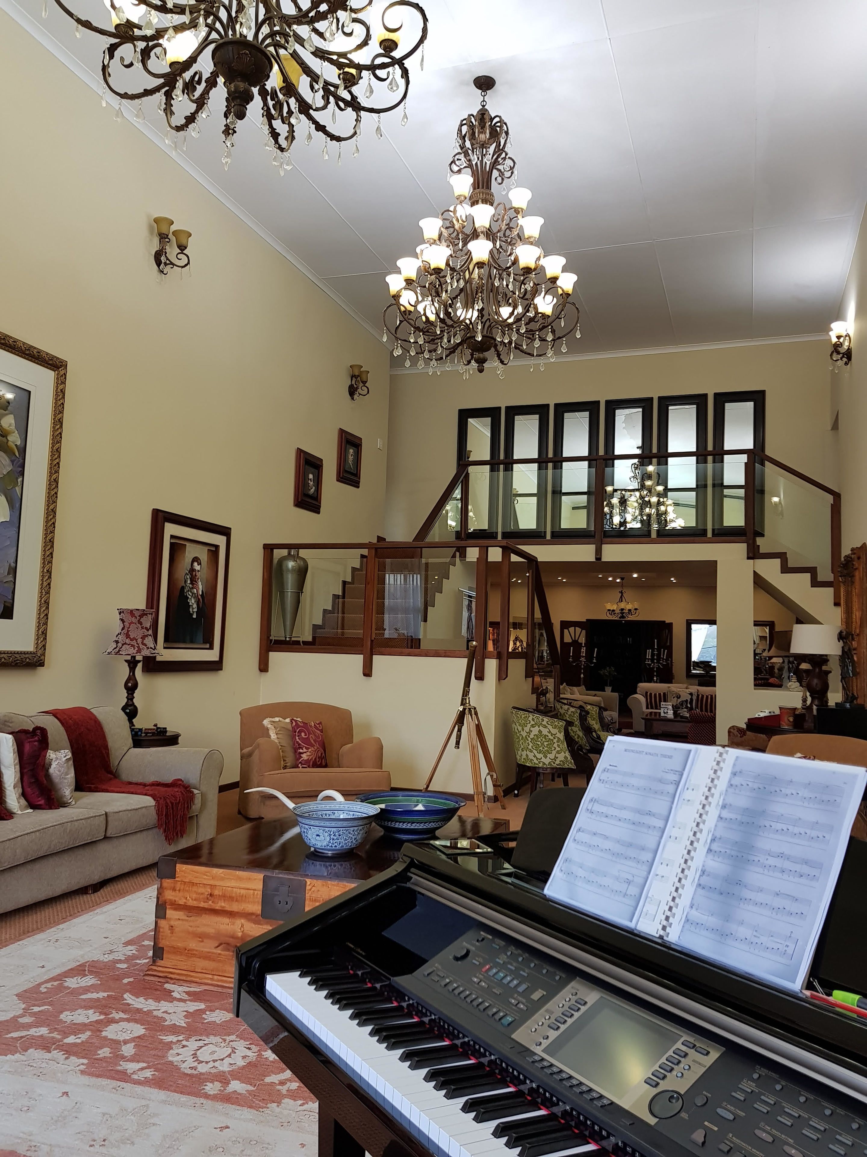 A spacious living room with a grand piano, a chandelier, and a staircase leading to an upper level.