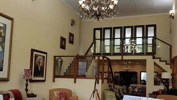 A spacious living room with a grand piano, a chandelier, and a staircase leading to an upper level.
