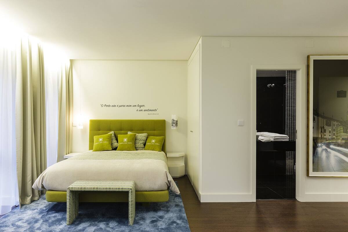 A hotel room with a bed, bedside table, and a view of the street through a window.