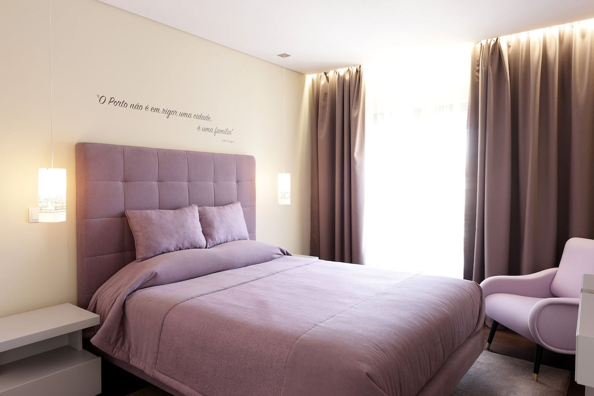 A bedroom with a large bed, a bedside table, a chair, and a wall with a quote.