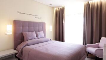 A bedroom with a large bed, a bedside table, a chair, and a wall with a quote.