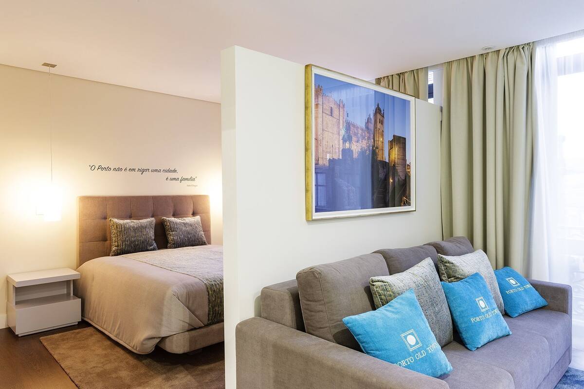 A hotel room with a bed, a sofa, a framed picture, and a quote on the wall.