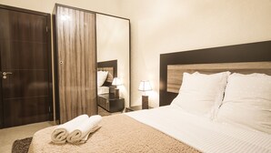 Hotellihuone, jossa on suuri sänky, vaatekaappi, peili sekä kaksi yöpöytää, joissa on lamput.