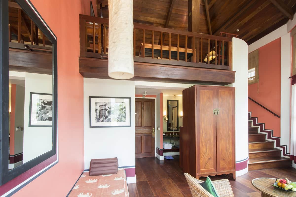 A spacious room with a wooden staircase, a large wooden cabinet, and a round wicker table with fruit.