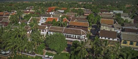 An aerial view of a coastal town with traditional buildings, palm trees, and a mountainous backdrop.