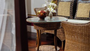 A wicker sofa with a glass table in front, a vase with flowers, and a view of greenery outside. - The Belle Rive Boutique Hotel (Luang Prabang)