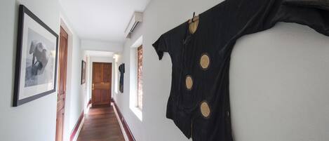 Un couloir au sol recouvert de planches de bois, avec des tableaux encadrés accrochés aux murs et un vêtement noir suspendu sur le côté droit.