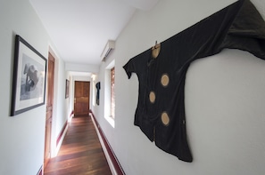 A hallway with wooden flooring, framed pictures on the walls, and a black garment hanging on the right.