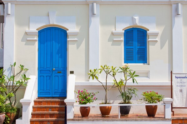 A building with a blue door and shutters, potted plants in front, and a sign indicating it is a hotel.