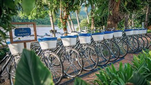 A row of bicycles with baskets, parked on a brick path with a sign indicating bicycle parking. - The Belle Rive Boutique Hotel (Luang Prabang)