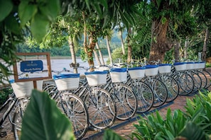 A row of bicycles with baskets, parked on a brick path with a sign indicating bicycle parking. - The Belle Rive Boutique Hotel (Luang Prabang)