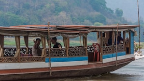 A traditional boat with passengers, featuring a covered deck and ornate railings. - The Belle Rive Boutique Hotel (Luang Prabang)