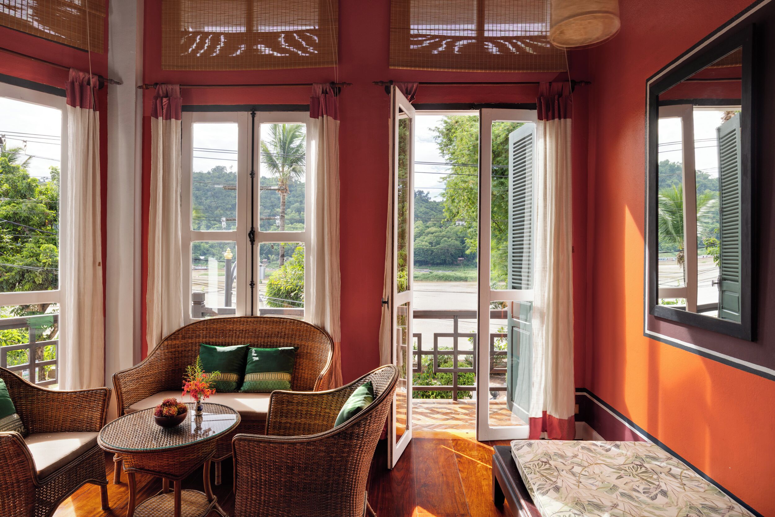 A room with wicker furniture, a glass table, and a view of greenery outside.